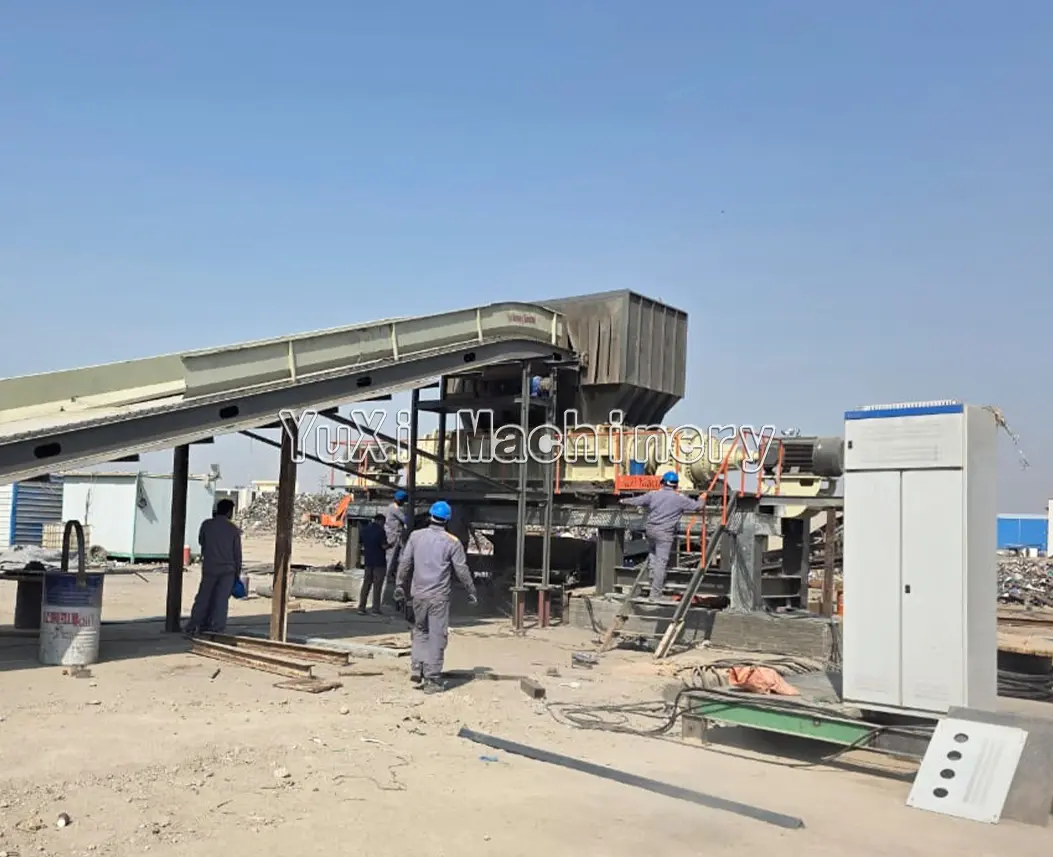 Workers installing a scrap metal shredding or processing line, including a large conveyor belt and hopper.